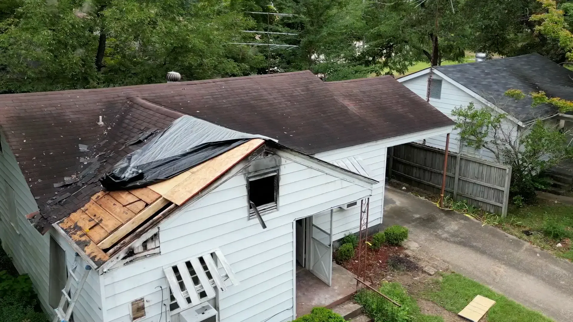 Storm-damaged house in Benton with a tarp over the roof breach and algae-streaked shingles